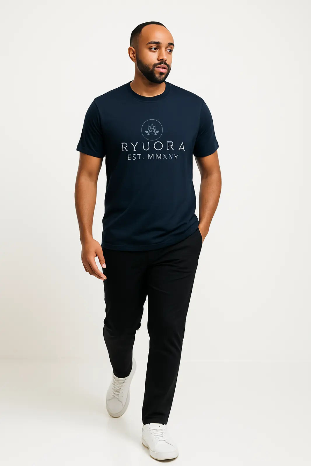 Man wearing navy Ryvora graphic t-shirt with black pants and white sneakers on white background