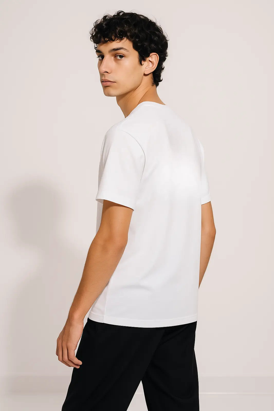 Young man wearing plain white t-shirt and black pants, posing against light background