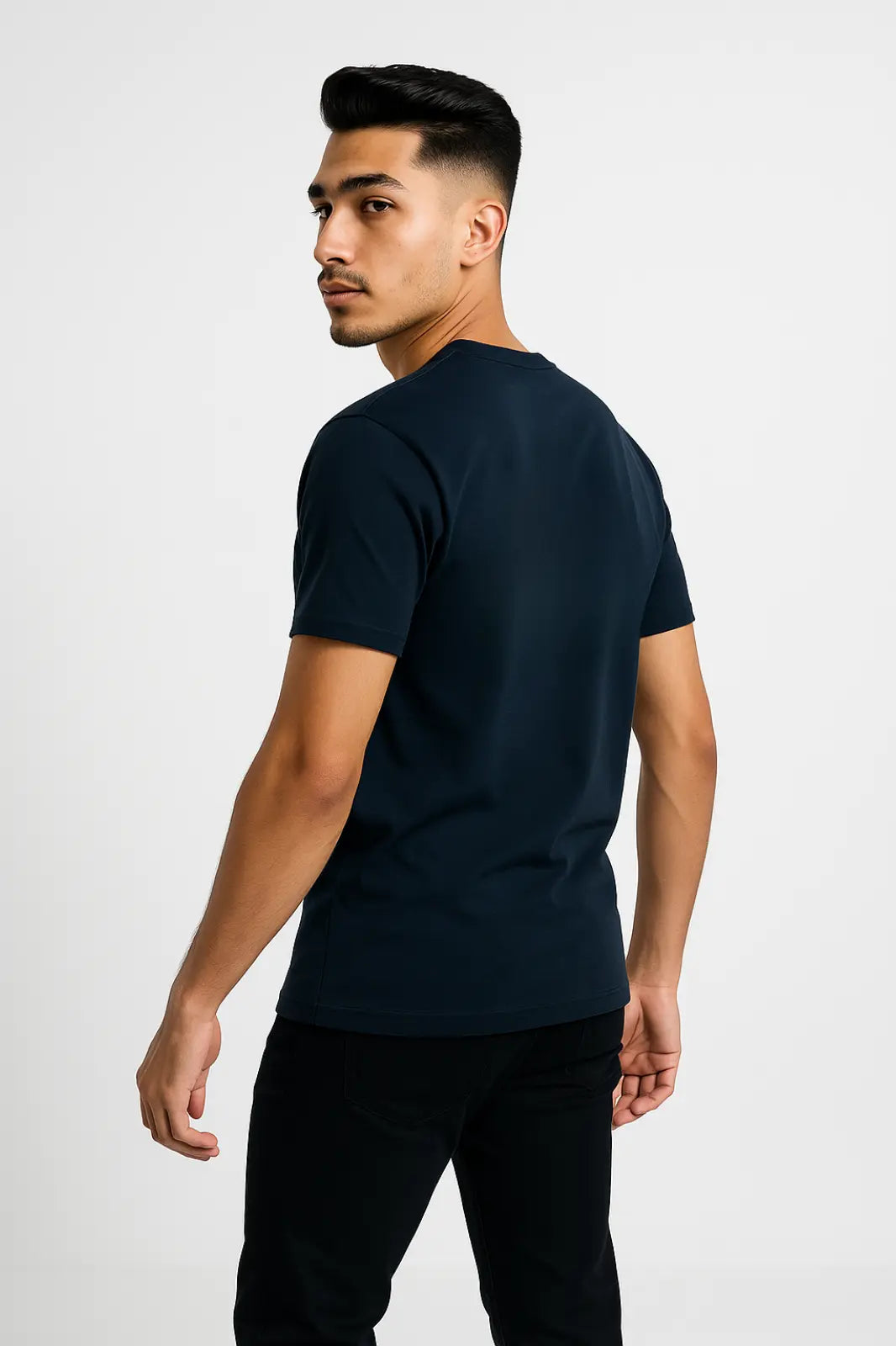 Young man in black jeans wearing a navy blue t-shirt, posing against a white background